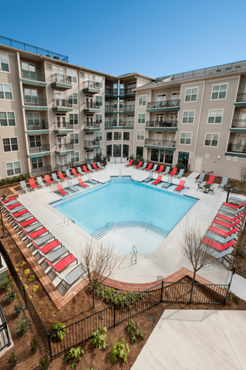 an aerial view of an apartment complex swimming pool with red chaise lounges